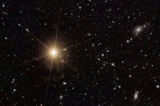 A smaller, close-up cutout from a larger frame featuring the galaxy cluster Abell 2764. It focuses on a bright star lying near to the cluster: V*BP-Phoenicis/ HD 1973, a star within our galaxy and in the southern hemisphere that’s nearly bright enough to be seen with the human eye.